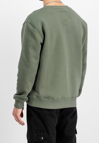 Bluza oliwkowa wykonana z miękkiej tkaniny, z klasycznym okrągłym dekoltem, ściągaczami na rękawach i dole, z małą prostokątną metką z tyłu.