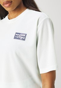 Ανοιχτό πράσινο mesh μπλουζάκι με στρογγυλή λαιμόκοψη, κοντά μανίκια και ορθογώνιο κεντητό λογότυπο που γράφει "Τένις" σε ναυτικό και λευκό χρώμα.