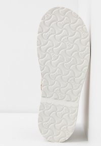 Semelle en caoutchouc blanc avec des motifs ondulés incurvés et un texte embossé répétitif "Birk", présentée en angle sur un fond blanc.