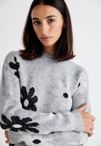 Grau gestrickter Pullover mit schwarz-weißen Blumenmustern, Rundhals, und gerippten Bündchen, aus weichem, strukturiertem Garn gefertigt.
