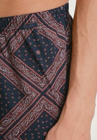 Navyblauwe stofshorts met een paisleypatroon in wit en maroon. Elastische tailleband met een label met de naam CALIDA. Zachte textuur.