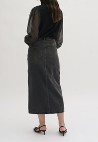 En mörkgrå denim midi kjol med en figursydd silhuett, två bakfickor och sydda detaljer. Kombinerad med transparenta svarta långärmar.