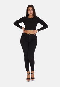 Zwart cropped top met lange mouwen en golvende zoom, gecombineerd met zwarte skinny jeans en zwarte sandalen met hak, met een aangesloten ontwerp.