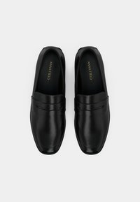 Par sorte læder slip-on loafers med firkantede tæer og "Anna Field"-mærke indeni, vist ovenfra på hvid baggrund.