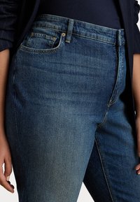 Sötétkék farmernadrág, slim fit szabással, közepes derékkal, öt zsebes dizájnnal és enyhe kopással a combokon.