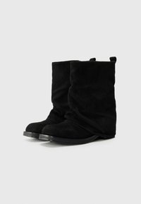 Botas de tornozelo em camurça preta com um design descaído, bicos arredondados e solas planas. Apresenta dois puxadores na gola.