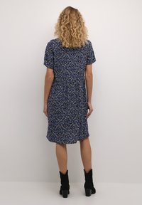 Rochie florală albastră cu mâneci scurte, croială lejeră și tiv până la genunchi. Botine negre cu toc completează ținuta.