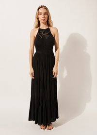 Vestido maxi negro con cuello halter, cuerpo texturizado con detalles de crochet abiertos, falda de capas fluida y sandalias planas.