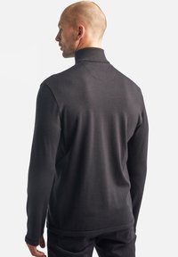 Mørkegrå langærmet sweater med høj krave. Blød tekstur, figursyet design og sømløse skuldre fremhæver en ren silhuet.