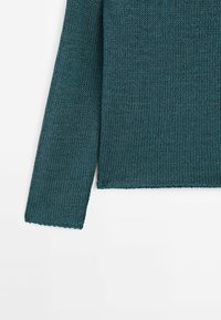 Manche et ourlet inférieur d’un pull en maille à manches longues de couleur sarcelle sur fond blanc, montrant un motif en tricot texturé et des bords droits.