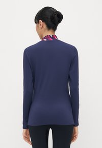 Marineblaues Langarmoberteil mit einem bunten gemusterten Kragen, aus glattem Stoff gefertigt, figurbetonter Schnitt und eleganter, minimalistischer Gestaltung.