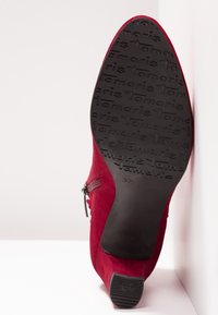 Botte à talon en daim rouge vue par la semelle, semelle extérieure en caoutchouc noir marquée "Tamaris", avec fermeture éclair latérale et taille 37 embossée sur la semelle.