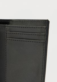 Μαύρο δερμάτινο πορτοφόλι με πολλαπλές θήκες για κάρτες και εμφανή ραφές. Λεπτό υφή και δομημένος σχεδιασμός χωρίς διακοσμητικά στοιχεία.