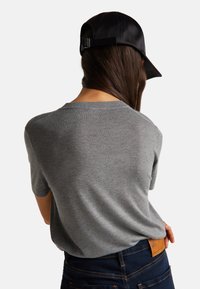 Šedý pletený svetr s krátkým rukávem a kulatým výstřihem, nošený s tmavomodrými džíny. Obsahuje černou koženou čepici s nastavitelným páskem.