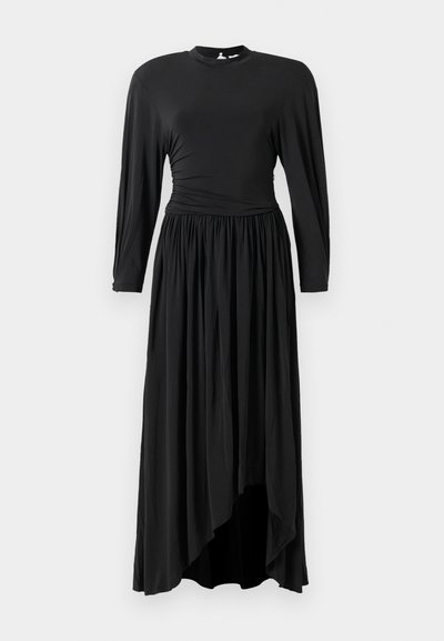 Ilga juoda suknelė, pagaminta iš minkštos medžiagos, su ilgomis rankovėmis, surinkta juosmens dalimi ir asimetriniu apvadu, suteikiančiu sruvenančią siluetą.