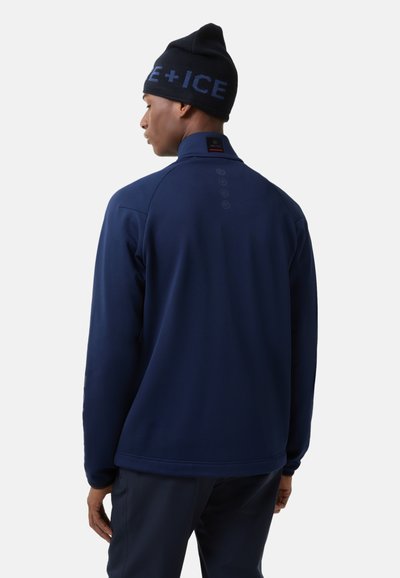 Granatowy polarowy sweter z wysokim kołnierzem, z logo i guzikami na plecach. Połączony z czapką z dzianiny w kolorze czarnym.