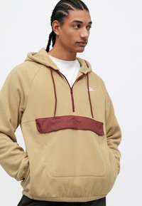 Taná fleece mikina s kapucňou a štvrťzipom, burgundská akcentová panel, šnúrky a klokaní vrecko. Mäký textil a uvoľnený strih.
