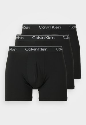 Trois paires de boxers noirs à design ajusté. Chacune a un logo "Calvin Klein" blanc sur la ceinture élastique.