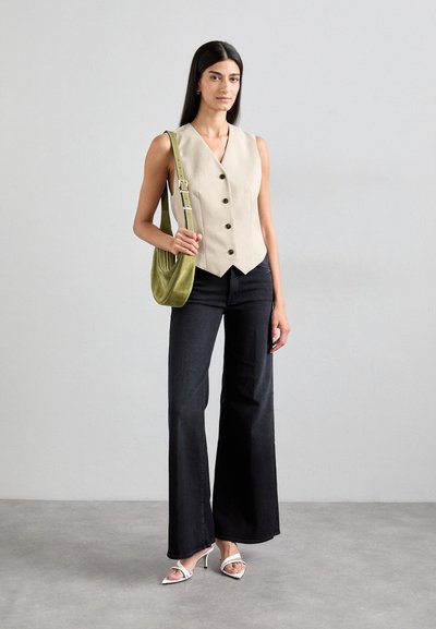 Beige sleeveless vest with buttons, paired with dark flared jeans. Accessory: green suede shoulder bag. White heeled sandals complete the look.