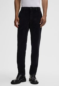 Dark corduroy trousers with a straight cut, featuring a front button closure, side pockets, and a soft, textured finish. Black leather shoes.