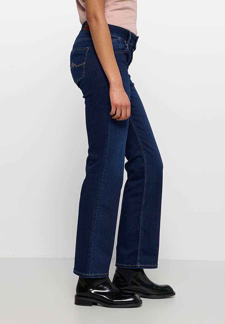 Dunkelblaue Jeans aus Denim mit geradem Bein, ausgestattet mit Gesäßtaschen und einer dezenten Nahtdetails. Kombiniert mit schwarzen, glänzenden Stiefeletten.