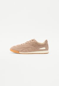 Beige semsket sneakers med en teksturert overflate, med en kremfarget mellomsåle og brun gummisåle. Inkluderer lisser og sideakenter.