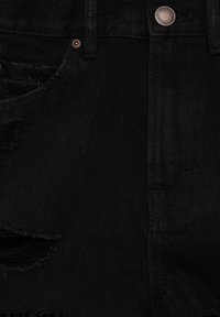 Jeans in denim nero con zone strappate, dotati di chiusura con bottone, hardware in rame e tessuto testurizzato. Inquadratura ravvicinata della parte frontale.