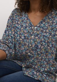 Bluse med blomsterprint i navy baggrund, letvægtsstof, V-hals og knaplukning. Blød tekstur med varierende blomster mønstre.