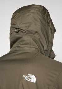 Veste vert olive avec une capuche ajustée, tissu texturé et le logo blanc "THE NORTH FACE" affiché en évidence au dos.