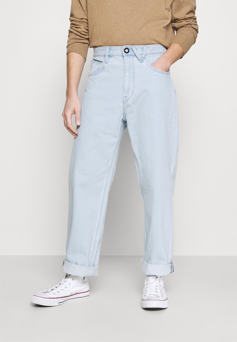Jean en denim bleu clair à coupe droite, ourlets retroussés, poches avant et fermeture par un seul bouton. Associé à des baskets blanches.