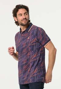 Heren polo in marineblauw met een oranje en paarse bladerenpatroon. Korte mouwen, kraag met contrasterende rand en zijsplitten voor extra comfort.
