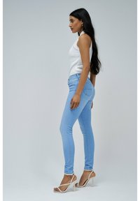 Jeans ajustados azul claro de denim, con un clásico diseño de cinco bolsillos y un sutil detalle de costura en el bolsillo trasero, combinados con una camiseta sin mangas blanca.
