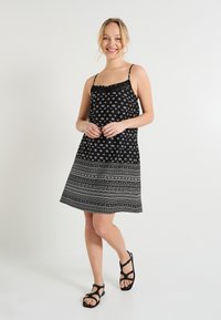 Vestido negro con tirantes finos, que presenta un diseño impreso de círculos y rayas horizontales, con un acento de encaje en el escote.