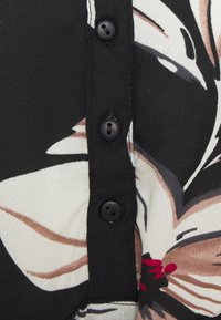 Svart knappad skjorta med blommönster i kräm, brunt och rött. Tyget är lätt och smidigt, med framträdande knappar.