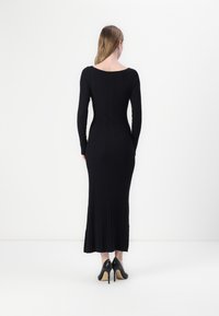 Black ribbed long-sleeve dress with a fitted silhouette, scoop back, and a floor-length hem. Worn with black high-heeled shoes.