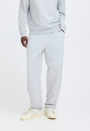 Hellgraue Jogginghose aus weichem Stoff. Verfügt über einen elastischen Bund mit Taschen und eine lockere Passform. Kombiniert mit hellfarbigen Sneakers.