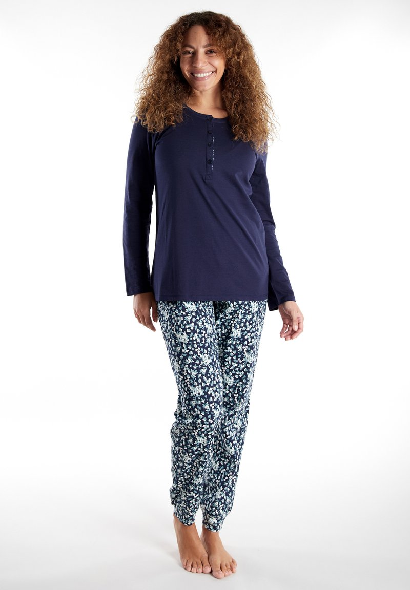 Marineblauw T-shirt met lange mouwen en knoopsluiting bij de hals, gecombineerd met bloemenpatroon broek in schakeringen van blauw, wit en groen. Zacht, casual materiaal.