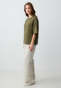 Olijfgroene linnen top met wijde mouwen, gecombineerd met licht gestreepte wijde broekspijpen. Zachte textuur en een relaxte pasvorm. Chunky witte platform schoenen.