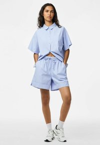 Gai�ši zils svītrains īsās piedurknes krekls ar pogu priekšpusi un vienu kabatu, kombinēts ar atbilstošām šortiem ar auklu un baltām sporta apavām.