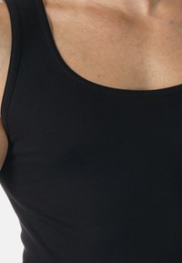 Czarny top na ramiączkach z okrągłym dekoltem i szerokimi otworami na rękawy, wykonany z gładkiego, elastycznego materiału. Posiada dopasowany fason.