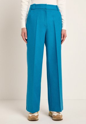 Blue wide-leg trousers made from a smooth fabric, featuring a straight cut, front pleats, and a high waistband. Worn with neutral sneakers.