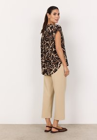 Kurzarmbluse im braunen und beigen Blattmuster. Kombiniert mit lockeren beigen Hosen und braunen, geflochtenen Ballerinas. Glatter Stoff, lockere Passform.