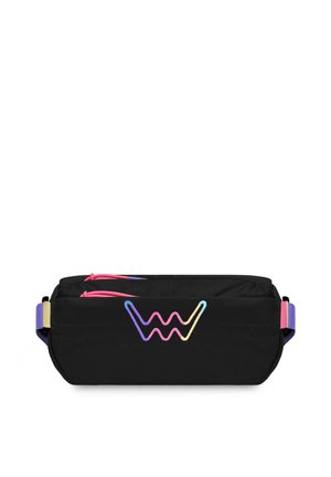 Black crossbody bag with colorful geometric accents, worn over a blue sweatshirt. Model stands outdoors with a green landscape in the background.