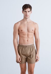 Pantaloni scurți din bumbac, cu croi lejer, ușori, de culoare maro, cu talie elastică. Au o deschidere frontală fără alte accesorii.