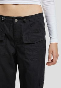 Svarta cargobyxor med elastisk midja, framfickor och sidocargofickor. Tillverkade av kraftigt tyg med synliga sömdetaljer.