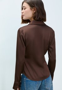 Brown satin shirt with a collar and long sleeves, featuring a smooth texture and slightly tailored fit, paired with blue denim jeans.
