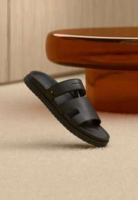 Μαύρα σανδάλια slide με λείο συνθετικό επάνω μέρος και δύο φαρδιές λουρίδες, λαστιχένια σόλα και μινιμαλιστικό σχέδιο.