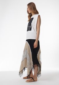 Top sin mangas blanco con un estampado gráfico negro; falda maxi plisada en capas en beige, negro y detalles de encaje; sandalias negras.