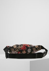 Černá květinová ledvinka s propracovanou červenou a zlatou výšivkou, s texturovanou tkaninou a nastavitelným černým popruhem pro bezpečné nošení.