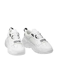 Baskets blanches avec des panneaux en maille, une semelle rembourrée et des accents noirs. La sangle avant affiche le logo "VERSACE JEANS COUTURE".